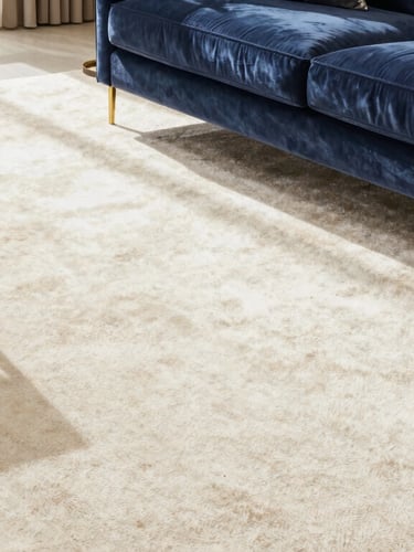 A bright, modern luxury living room with pristine cream carpets and a velvet sofa, natural daylight streaming in, architectural lens