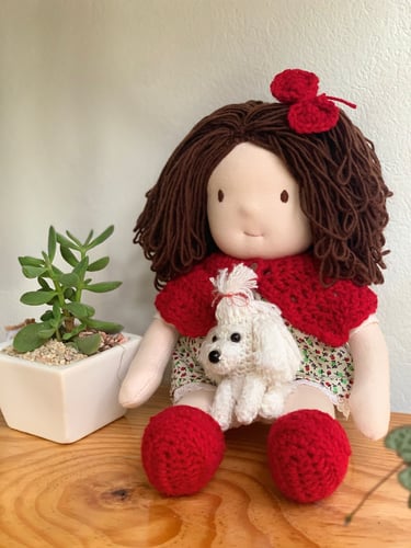 Muñeca de tela hecha a mano con cabello de estambre castaño, sosteniendo un perrito blanco tejido