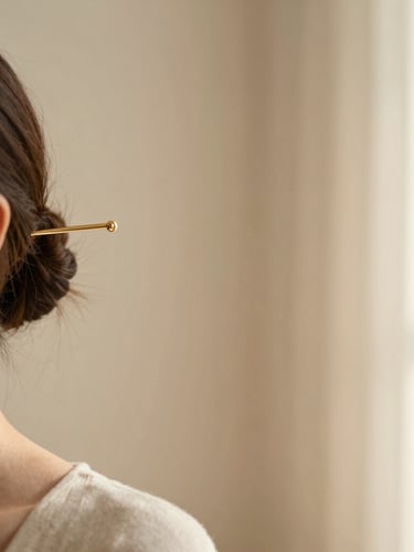 A soft-focus lifestyle shot of a woman wearing a minimalist gold hair pin, warm morning light casting gentle shadows on a beige wall, 35mm