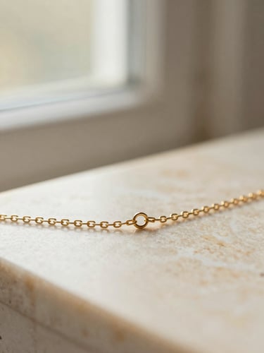 Macro close-up of a delicate gold chain resting on a warm alabaster surface, soft morning window light, shallow depth of field, 35mm