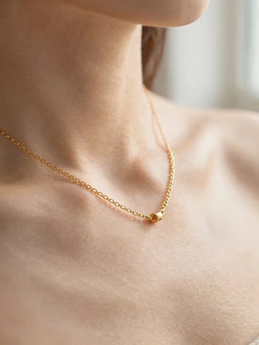 Macro close-up of a delicate gold chain necklace resting on sunlit skin, soft morning window light, warm beige tones, shallow depth of field, 35mm