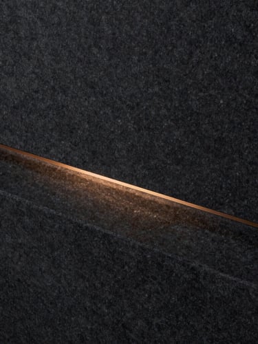 Macro shot of dark charcoal stone with a single warm bronze linear light reflection, minimalist architectural detail, 35mm