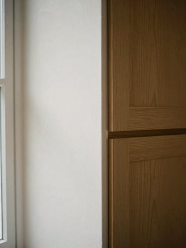 Tight detail shot of custom oak cabinetry meeting a smooth plaster wall with an uncompromisingly clean joint, soft natural light, 35mm film.
