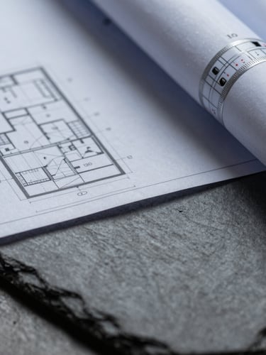 A close-up macro shot of architectural blueprints resting on a dark slate surface, sharp shadows, cool diffused daylight.