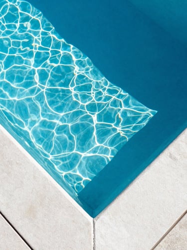 Top-down architectural view of a pristine, crystal-clear swimming pool, sharp geometric concrete lines, deep blue water with light caustics from bright midday Florida sun, 35mm lens.