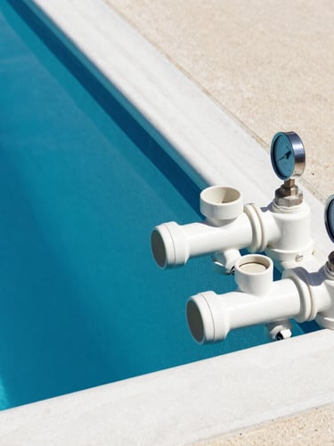 Crisp architectural pool photography, bright midday sun, deep blue water, clean geometric lines, close-up of clean PVC pipe manifolds and pump gauges on the right side of the frame, 35mm lens