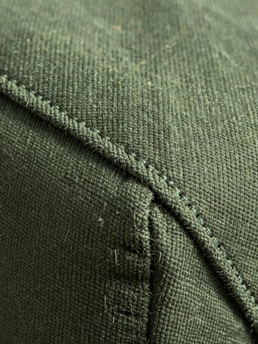 Extreme macro shot of heavy-duty pine green canvas fabric, showing rugged double-stitch seams and natural fiber texture under crisp morning light.
