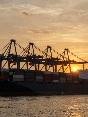 Wide-angle epic shot of massive container ship docked at Tanjung Priok port during a dramatic amber golden-hour sunrise, industrial cranes silhouette against the glowing sky