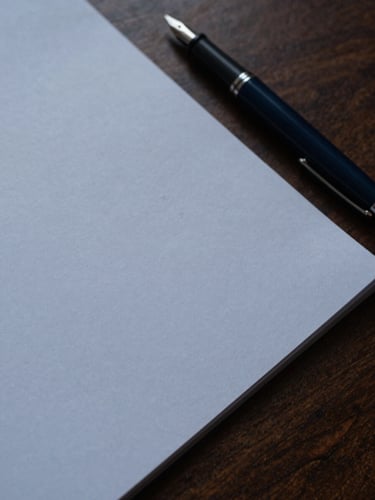 Close-up of a heavy textured paper document and a fountain pen resting on a dark walnut desk, soft side lighting, moody financial editorial style.