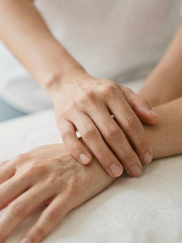 Close-up of therapeutic touch, hands resting gently on a wrist, warm editorial photography, soft diffused daylight, muted beige tones, shallow depth of field, 35mm
