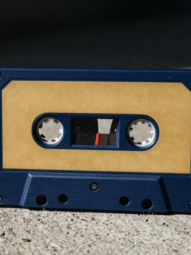 A close-up of a vintage cassette tape painted in blue and gold on raw concrete, dramatic direct sunlight, high-contrast streetwear photography, 35mm film grain.
