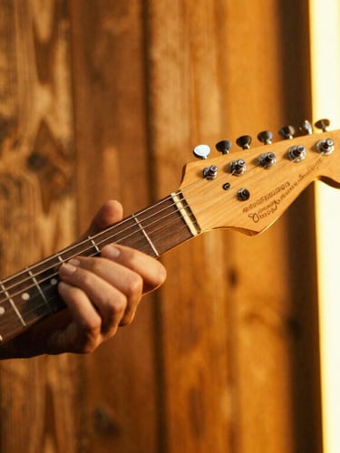 Close-up of an electric guitar neck and hands playing under warm amber stage lights, weathered wooden background, shallow depth of field, 35mm film.