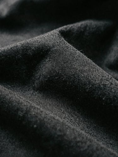 Macro close-up of 280gsm organic cotton knit texture, high-contrast directional light, deep shadows, desaturated dark tones, 35mm film grain