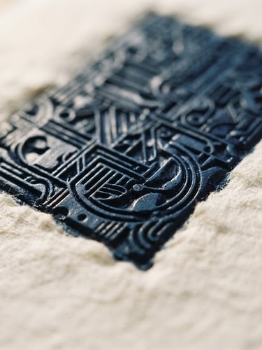 Macro close-up of a heavy letterpress printing plate with fresh dark blue ink, showing the deep texture of thick cotton paper, warm window side-light, shallow depth of field, 35mm.