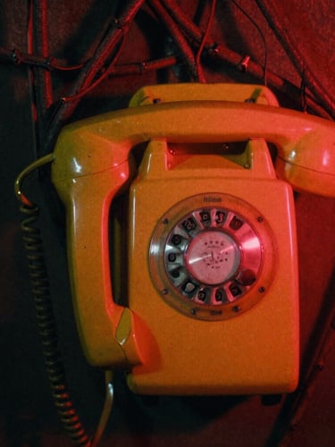 Extreme close-up of dark, pulsing vines wrapping around a retro yellow wall telephone, illuminated by a flickering red neon light, heavy film grain