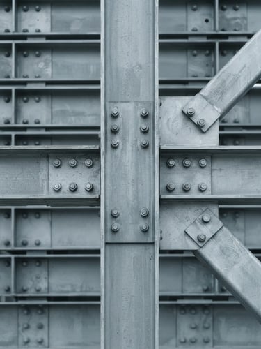 Orthographic close-up of a structural steel joint, desaturated cool grey tones, crisp overcast daylight, minimalist architectural photography, sharp focus
