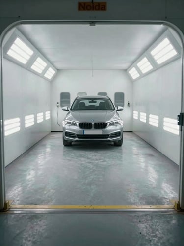 Wide environmental shot of a clean, organized Noida workshop bay with a car positioned inside a modern, brightly lit pressurized paint booth.