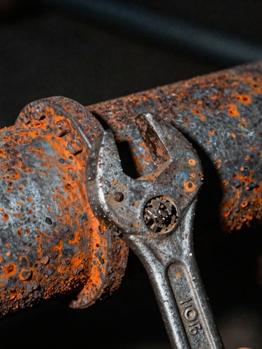 Extreme close-up of a rusted steel pipe being tightened by a heavy wrench, harsh direct flash, gritty texture, dark background.