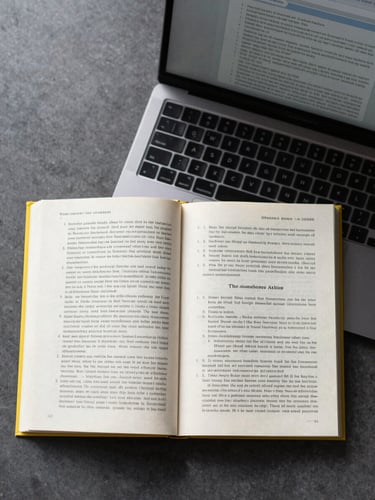 Top-down flat-lay of an open textbook with clean yellow highlighting next to a modern laptop displaying a structured document, bright morning daylight.