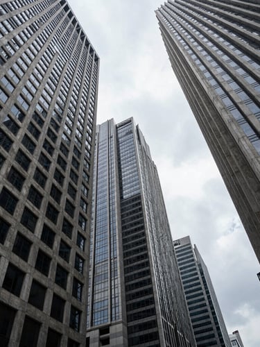 Low-angle architectural photograph of Jakarta's financial district skyscrapers, sharp concrete and steel geometry cutting into an overcast sky, high-contrast dramatic shadows, cold corporate editorial style.