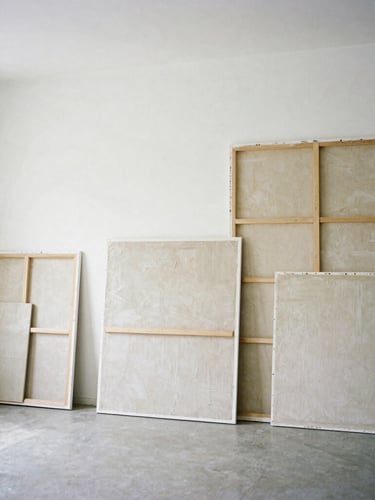 Wide environmental shot of an empty, sunlit art studio, high ceilings, large-scale textured canvases resting against pristine white gallery walls, soft diffused natural daylight