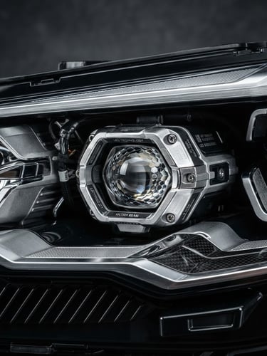 Premium macro product photography of a pristine car headlamp, crisp studio strobe lighting, high-contrast dark grey background, sharp metallic textures