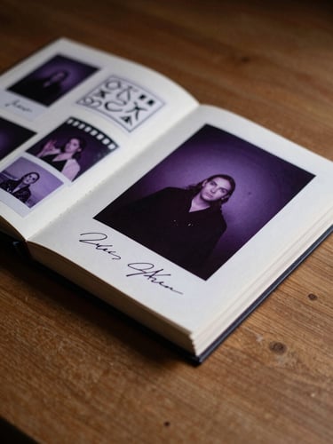 Macro shot of a hand-bound photo album open on a wooden table, showing custom stickers, hand-written signatures, and photo booth strips under warm side-lighting.