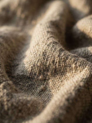 Macro portrait shot of heavy oatmeal-colored linen fabric, showing deep shadows in the raw flax weave under low-angle afternoon window light.