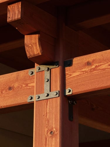 Close-up architectural shot of interlocking redwood joinery, clean black iron hardware, warm golden-hour California light highlighting natural wood grain, 35mm.