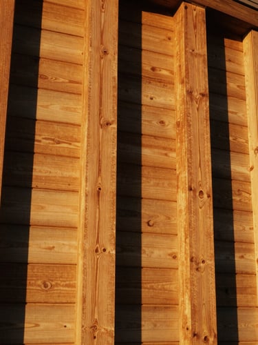 Low-angle architectural shot showing structural alignment of redwood posts and horizontal boards, warm golden-hour California sunlight, rich golden-brown wood tones, 35mm