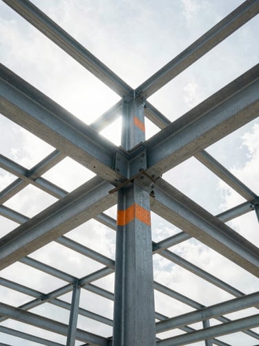 Low-angle heroic shot of exposed steel framing against bright Florida daylight, sharp structural geometry, safety-orange markings visible