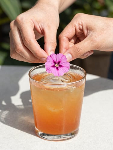 A close-up shot of hands carefully placing an edible pink wildflower garnish on a vibrant amber cocktail, soft sun-dappled lighting, outdoor garden setting, 35mm
