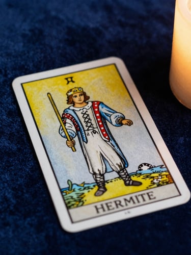 Overhead shot of a single Tarot de Marseille card, L'Hermite, resting on dark blue velvet, illuminated by soft golden candlelight from the side, extreme close-up, dramatic shadows.