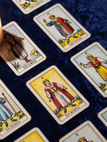 Overhead flat-lay of historic Tarot de Marseille cards resting on deep midnight blue velvet, soft warm side lighting from a single candle casting long dramatic shadows, tactile texture of aged paper.
