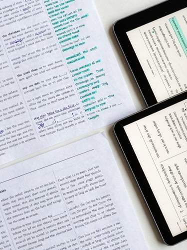 Overhead desk study of structured lesson plans, marked-up English texts with precise technical teal annotations, and a digital tablet showing grammatical patterns.