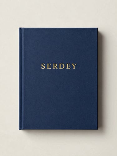 A beautifully bound art book cover with minimalist typography and gold foil details, resting on a clean marble surface, soft gallery lighting