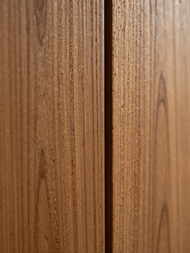 Extreme close-up macro shot of engineered wood panel texture, showing fine natural grain under dramatic side lighting, warm bronze tones, shallow depth of field.