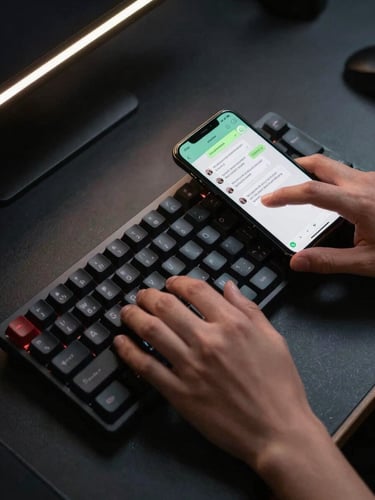 Close-up overhead shot of hands typing on a dark mechanical keyboard, a phone screen beside it showing a WhatsApp thread with automated reply timestamps, single high-contrast rim light from the upper left casting sharp shadows, dark workspace surface with faint data reflections, no faces visible