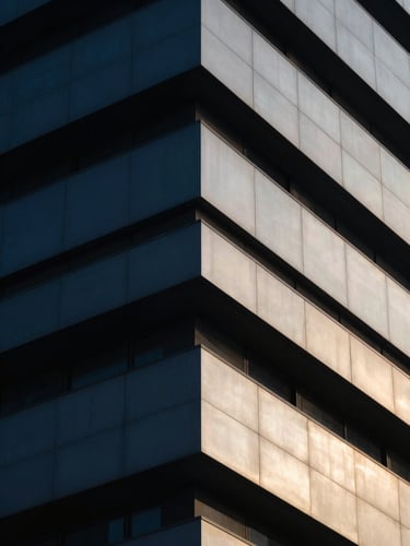 Abstract architectural geometry of a modern futuristic building corner, sharp lines, deep blue shadow and bright gold sunlight reflection, cool crisp focus
