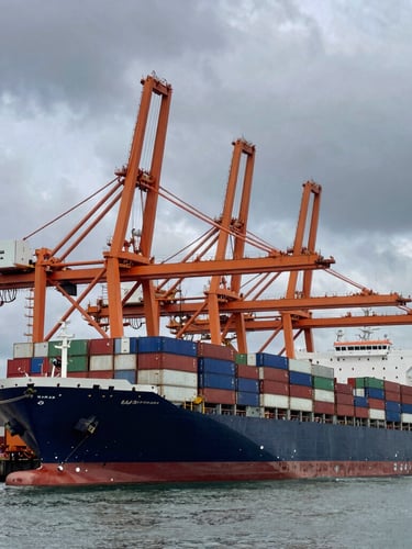 Wide-angle high-contrast shot of a massive container vessel docked at a modern industrial port, giant orange gantry cranes loading cargo under a dramatic overcast maritime sky.