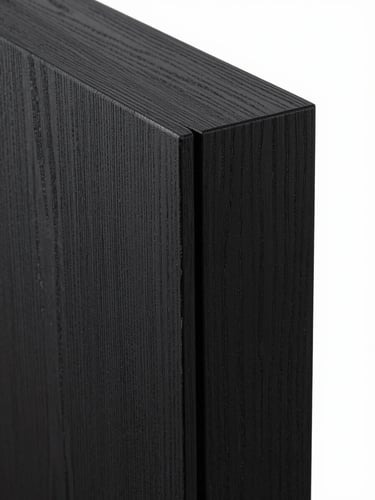 Tight close-up of a custom joinery corner detail — two panels of blackened oak meeting at a precise mitered edge, a shadow gap revealing the depth of the reveal, studio lighting raking across the surface to show grain texture and finish quality, no people, no props
