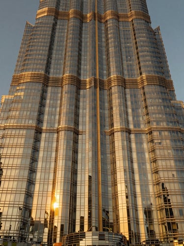 Symmetrical wide-angle architectural photograph of a soaring modern glass skyscraper in Dubai, dramatic golden-hour sunlight reflecting off the facade, warm metallic tones, sharp focus, 35mm
