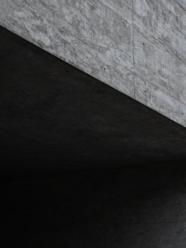 Architectural detail of a minimalist concrete structure with sharp geometric shadows, clean lines, low-key lighting