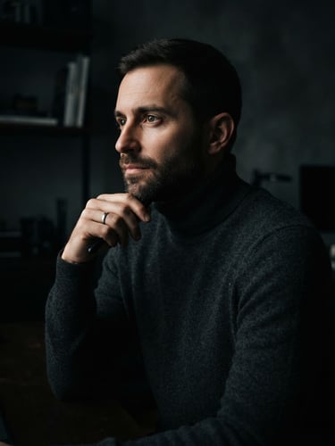 Low-key studio portrait of a designer in a dark charcoal turtleneck, sharp side lighting, deep shadows, premium editorial style.