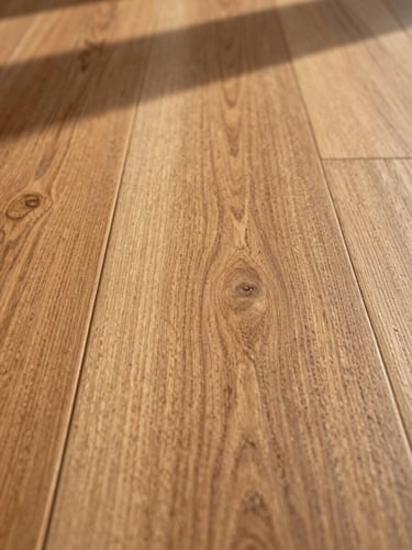 Extreme close-up of oak hardwood flooring, tight framing on the grain and beveled edge detail, warm north-facing daylight raking across the surface to reveal natural wood texture and finish, right side of frame
