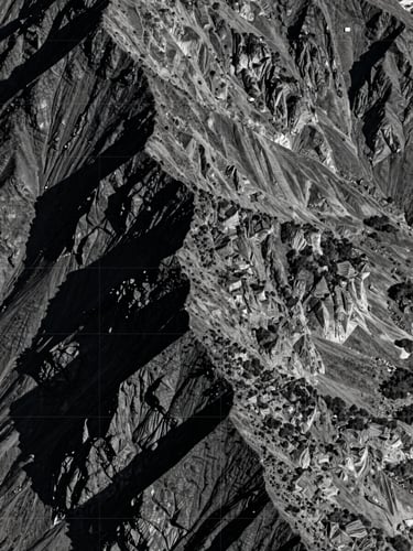 High-resolution satellite monitoring view of a rugged mountain ridge, sharp shadows, technical coordinate lines overlay, deep slate tones.