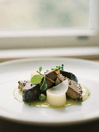 A close-up of an artfully plated seasonal dish under soft, natural window light, muted olive and ivory tones, shallow depth of field, 35mm photography