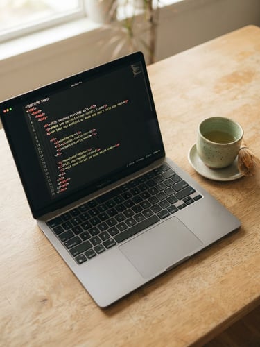 Overhead view of a sleek laptop displaying clean HTML structure next to a ceramic teacup on a warm cream desk, soft natural daylight