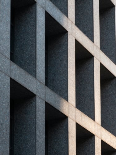 Abstract close-up of a modern granite building facade, sharp architectural lines, deep shadows, cool morning light.