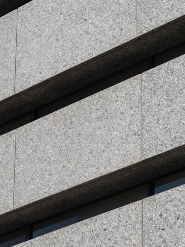 Abstract close-up of a modern granite building facade, clean sharp shadows, architectural lines, cool stone gray tones.